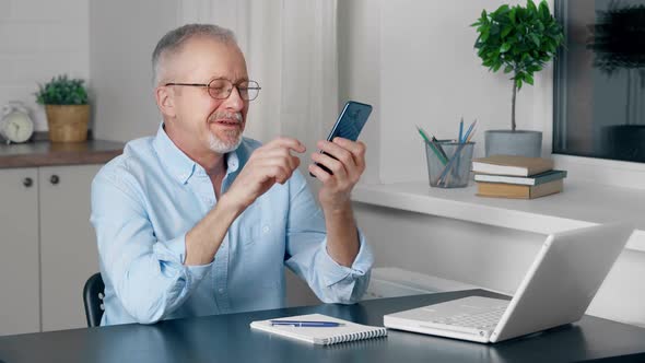 An Elderly Person is Talking on the Speakerphone of a Mobile Phone