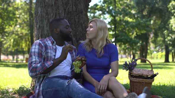 Mixed Race Couple Eating Grapes in Park and Speaking, Spending Time Together alt