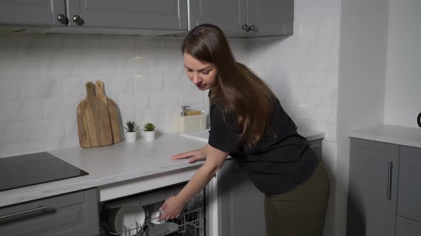 Young Woman in the Kitchen Opens the Dishwasher Loads and Takes Out Dishes