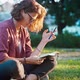 A Young Woman Sitting on the Lawn in the Park and Making Notes in Her Notebook - VideoHive Item for Sale