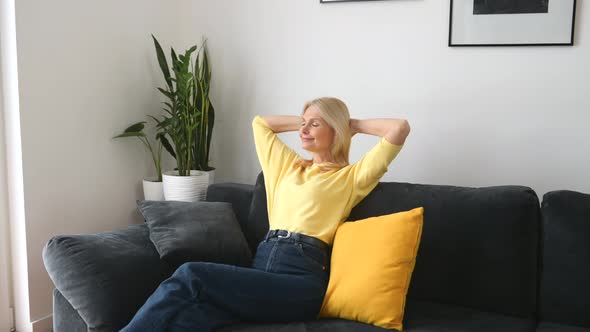 Lighthearted Positive Middleaged Woman with Long Hair at the Sofa in Modern Apartment