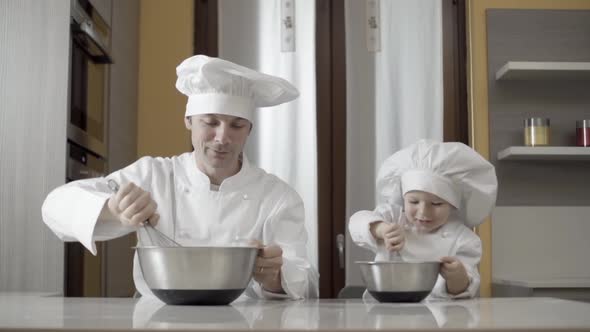 Dad and Son Mixing Food Ingredients in Steel Bowl in Their Home Kitchen alt