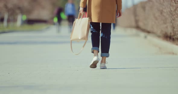 Woman Walks Along a Park Path in Sneakers and with a Bag alt