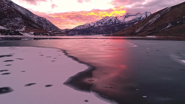 Flying over lines of ice and snow on frozen lake during colorful sunset alt