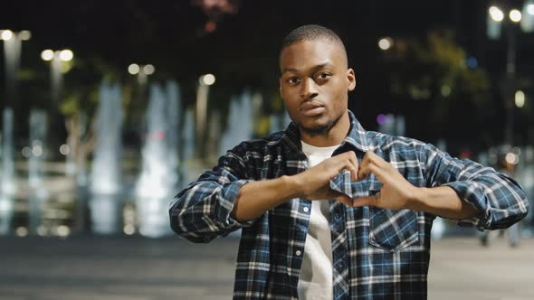 Friendly Kind African American Young Man Guy Shows Shape of Heart with Hands Fingers Looks Inside alt
