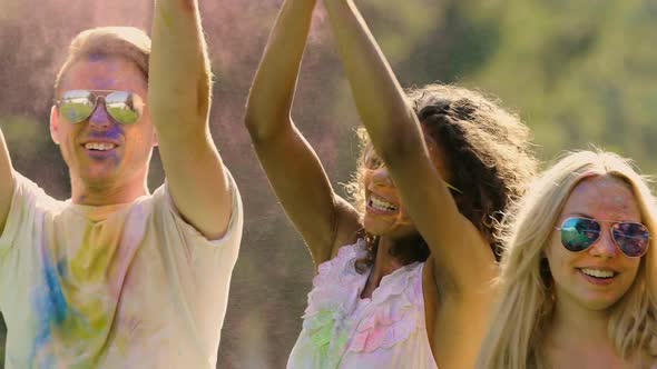 Happy Best Friends Dancing and Jumping in Colorful Dust Clouds at Holi Festival alt