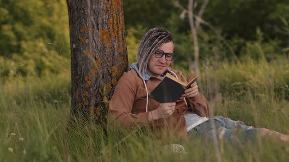 A Man in Casual Clothes and Glasses Reads Literature Under a Tree alt