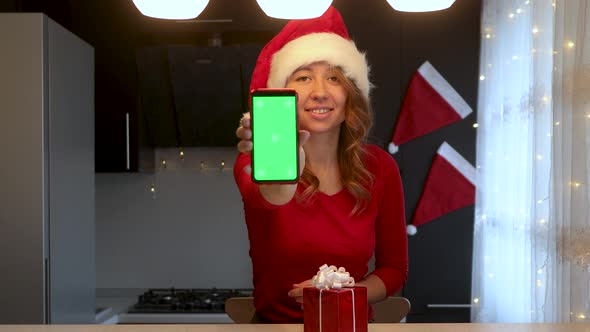 A girl in the kitchen talks by video call and shows a smartphone with a green screen alt