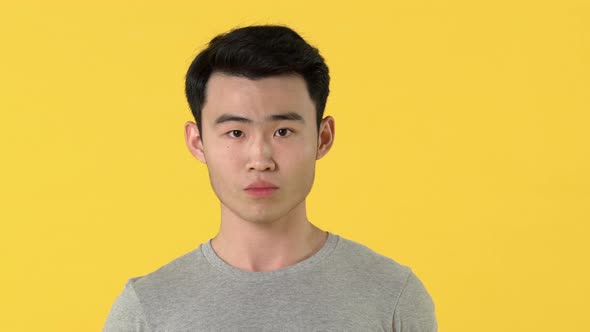 Portrait of sad young asian man crying in front of camera against yellow background