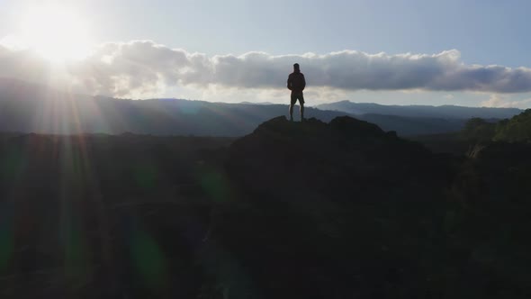 A Man Standing on a Mountain Peak in Rays of Evening Sun