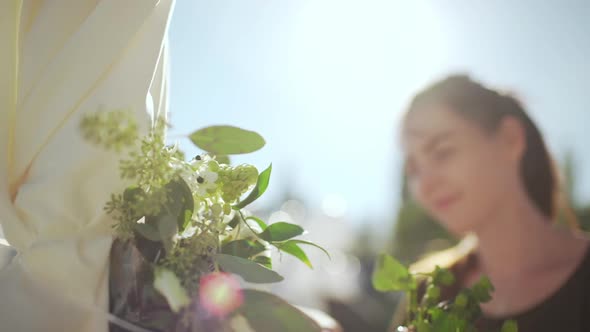Browhaired Female Decorating Wedding Arch with Flowers in Slowmotion alt