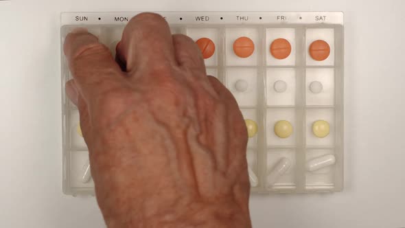 Senior male hand takes a pill from a plastic pill organizer