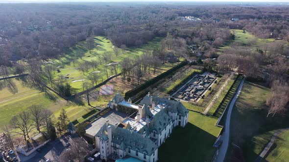 An aerial view over an upscale, luxury mansion with an eight reflection pool fountain, on Long Islan alt