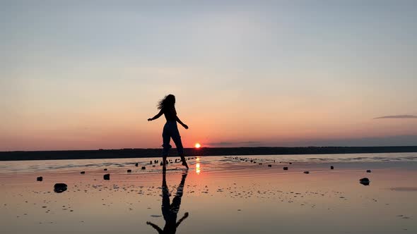 Silhouette of a beautiful woman dancing in the background of the sunset in the water.
