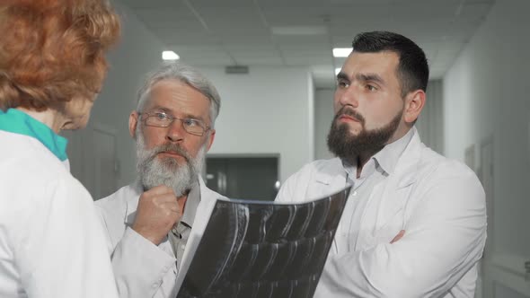 Two Male Doctors Discussing MRI Scan of a Patient with Their Female Colleague