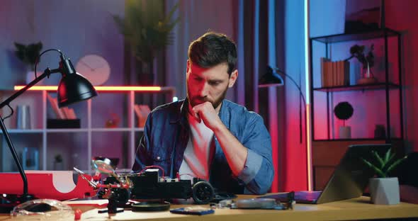 Man Watching at Disassembled Toy Car on the Table and Trying to Repair it with screwdriwer alt