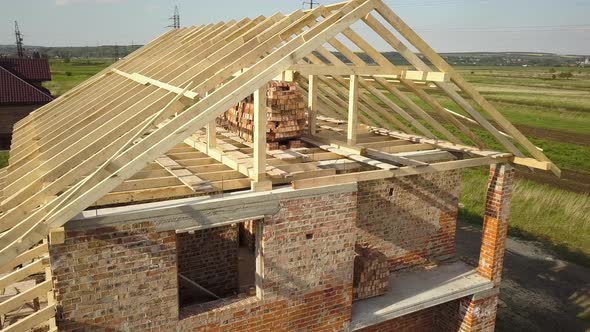Aerial view of unfinished brick house with wooden roof frame structure under construction alt