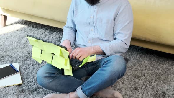Man Working at the Computer with a Lot of Reminder Notes Sitting Near Sofa alt