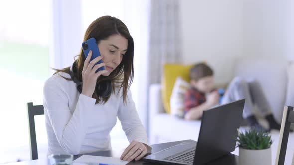 Single mother working at home office with son in background alt