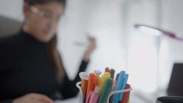 A Young Student From Colombian Universitary Sitting at a Table and Picks Up a Pen From Pen Stand on alt