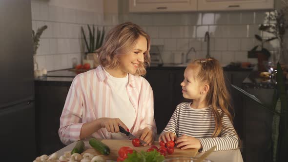 Cute Mom Teaches Her Little Daughter How To Make Fresh Vegetable Salad in Her Kitchen at Home alt