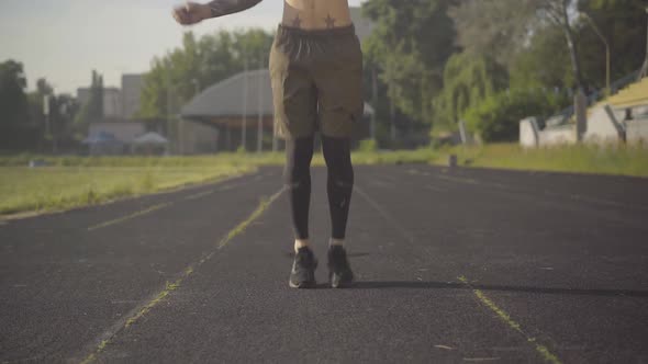 Front View of Young Caucasian Sportsman Jumping Rope on Athletic Field. Portrait of Concentrated Man alt