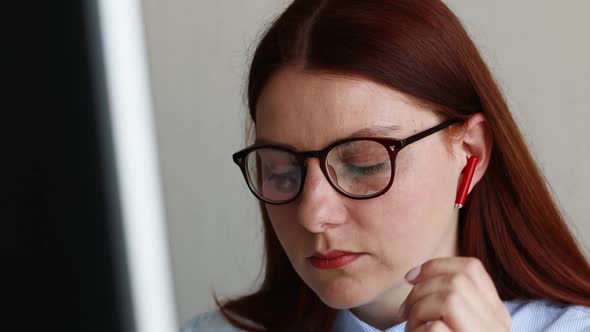 Caucasian Young Business Woman in Wireless Headphones with Eyeglasses Watching a Webinar Listening alt