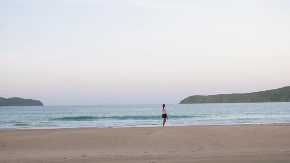 Young woman walking barefoot in the sand in the distance at dusk on Nacpan Beach, Palawan, the Phili alt