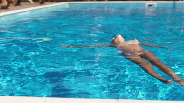 A Girl in a Pink Swimsuit with Glasses Lies on the Water in the Pool on Her Back and Enjoys the alt