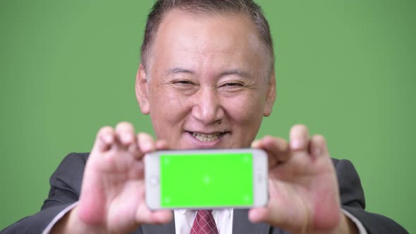 Mature Japanese Businessman Showing Phone To Camera alt
