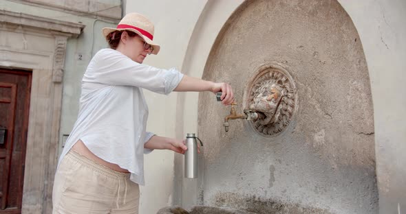 Woman filling a drinking bottle at ancient fountain