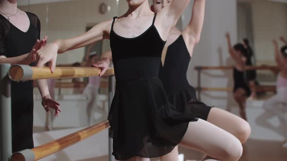 Two Little Girls Training Near the Stand in the Ballet Studio and Their Coach Fixes the Position of alt