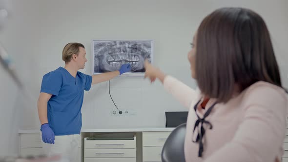 Male Dentist In Dental Office Shows Patient Image Of Her Teeth On Big Screen alt