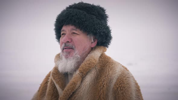 Old Asian Man Admiring Beauty of Northern Nature Standing on Snowy Ice Outdoors Looking Away alt