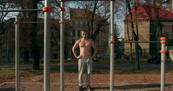 Young Man Is Standing Near Horizontal Bars After Training in Sunny Weather  alt