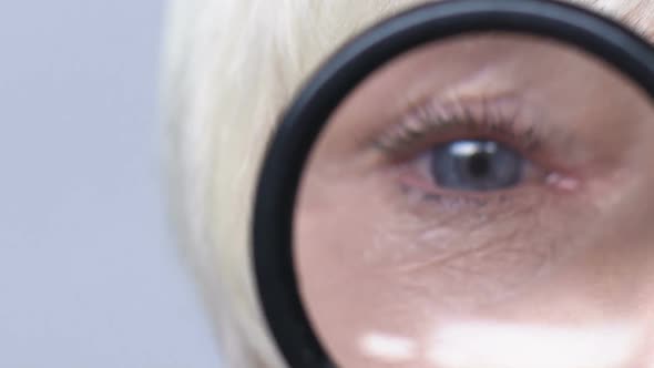 Doctor Examining Mature Woman Eyes Through Magnifying Glass alt