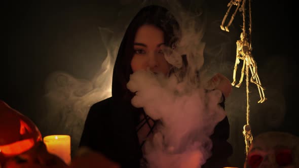 A Young Pretty Woman in a Black Mantle with Gothic Makeup is Smoking an Electronic Cigarette alt