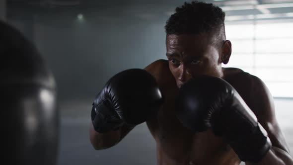 African american man wearing boxing gloves training in empty building punching punchbag alt