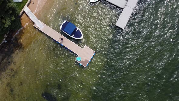 Overhead drone shot of a man walking back to shore from a dock at Lake Payette in McCall, Idaho. Thi alt