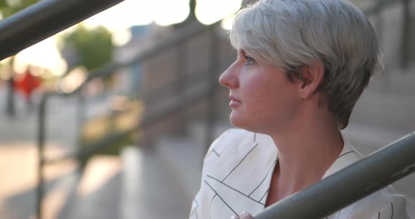 Strong beautiful women in fun fashion striped white suit jacket top sitting on stairs leaning agains alt