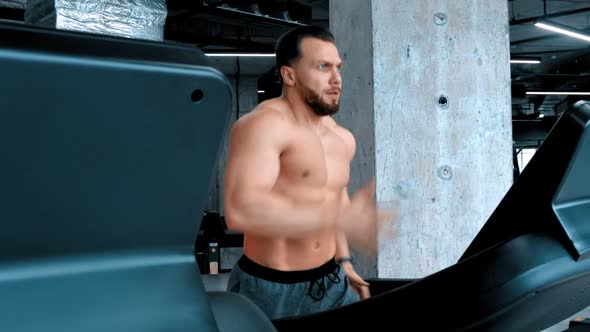 A Bearded Attractive Man Bodybuilder Running on the Treadmill with an Effort alt
