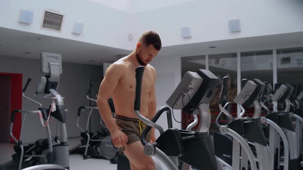 The Man Warms Up His Muscles on the Elliptical Bike in the Gym alt