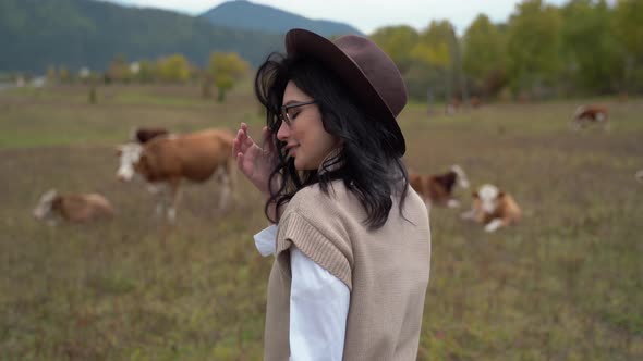 Beautiful Girl with Black Hair in Glasses Walks Around Ranch with Cows alt