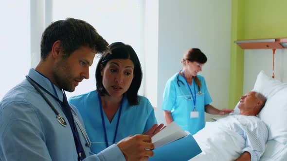 Doctors discussing on reports while nurse interacting with patient in background alt