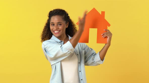 Young African American woman looking at and pointing to house cutout model