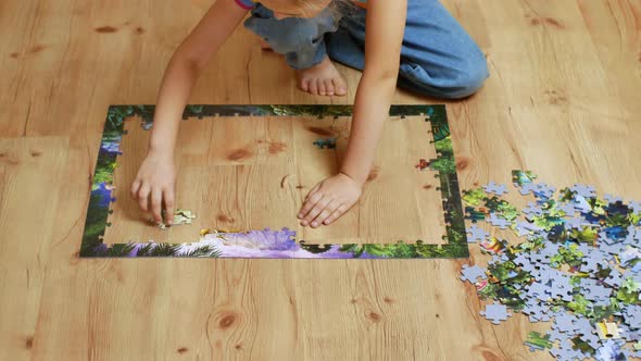 A Beautiful Little Girl Assembles a Complex Puzzle on a Wooden Floor alt