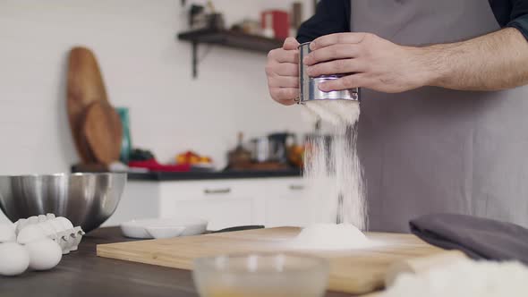 The chef in an apron kneads the dough. Close-up of a cook's hand. Flour is scattered on the table alt