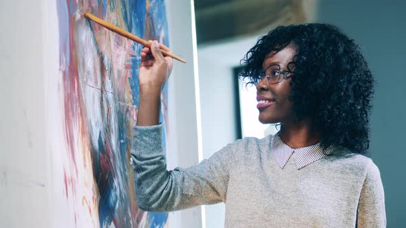 Smiling African Ethnicity Woman is Using a Brush to Finish a Painting alt