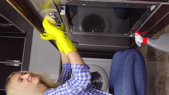 woman in yellow rubber protective glove cleans gas stove with yellow sponge. alt