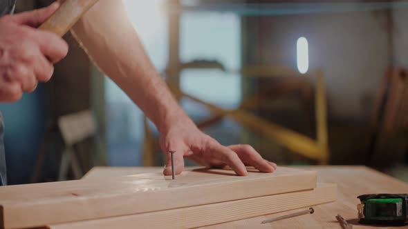 Closeup Shot of Man Driving a Nail with a Hammer in a Wood Board in a Studio